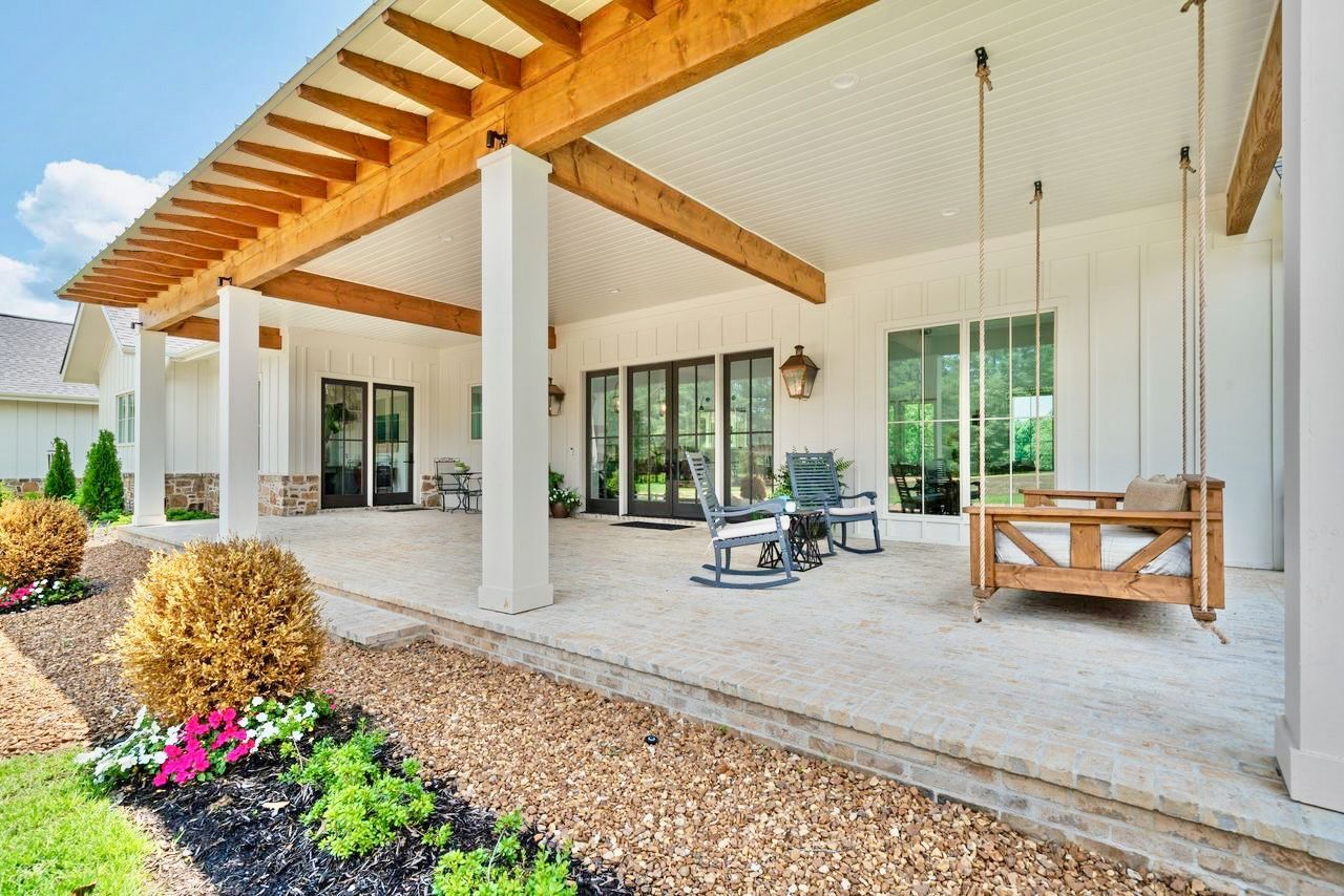 Covered patio with white pillars, wood beams, a swing, and black-framed doors.
