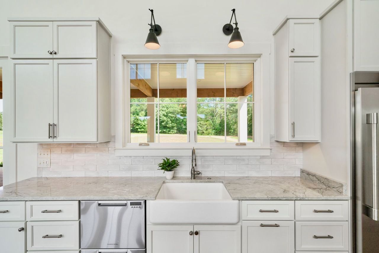 White kitchen with sink under window, cabinets, granite countertop, and small appliances.