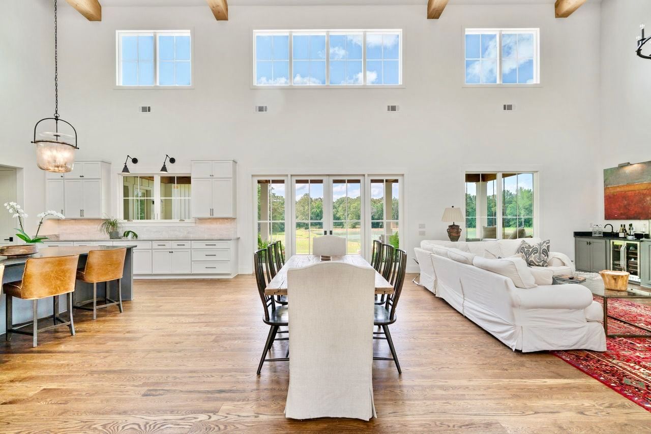 Open-concept living space with dining area, kitchen, and living room large windows and skylights, white walls, wooden beams, and hardwood floors.
