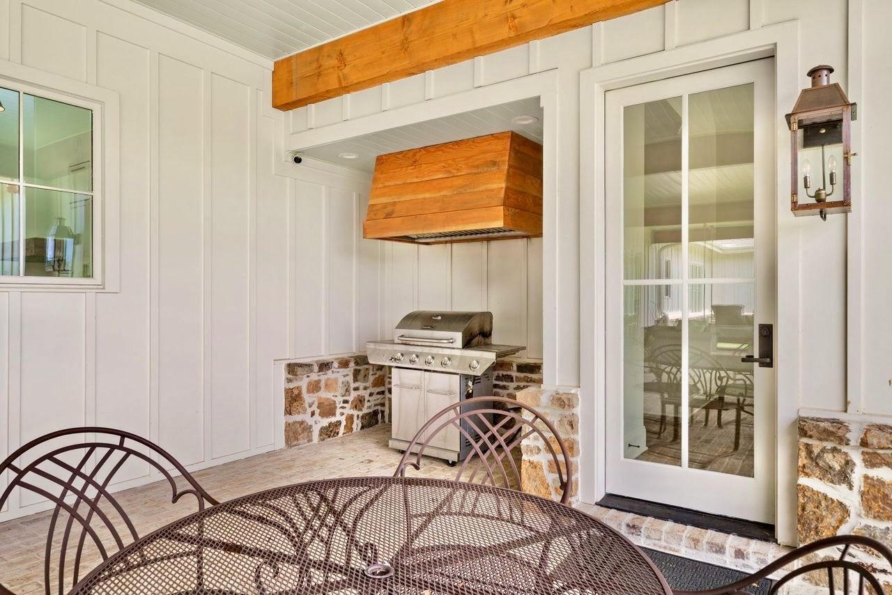 Outdoor kitchen with grill, stone accents, wooden hood, and patio table.