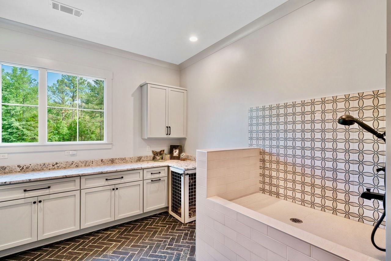 Dog wash station in bright room with window and storage. Features white cabinets, tile, and a patterned floor.