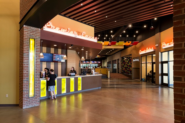 A lobby of a movie theater with people standing at a counter.
