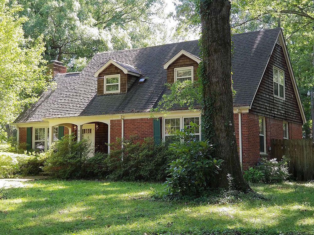 Exterior (Before) - Red brick house with dormers, shutters, and a tree in the yard.