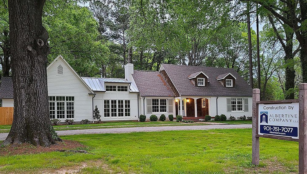 Exterior (After) - White house with brick roof, dormers, and windows, set among trees.