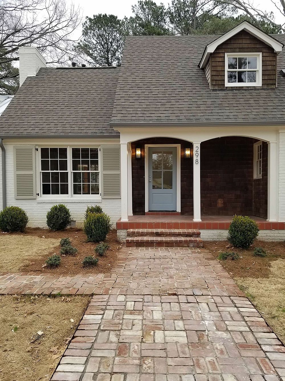 Exterior (After) - Cottage-style house with brick walkway, white siding, brown roof, blue door, and small shrubbery.
