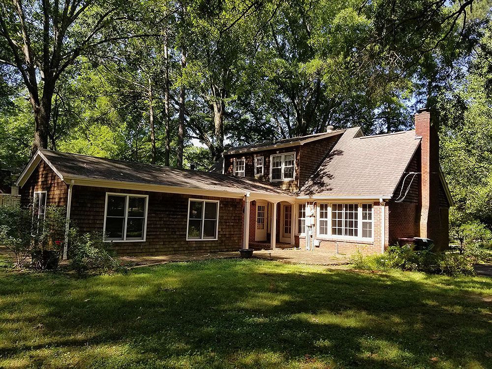 Exterior (Before) - Brick house with a chimney and windows, surrounded by trees and a green lawn.