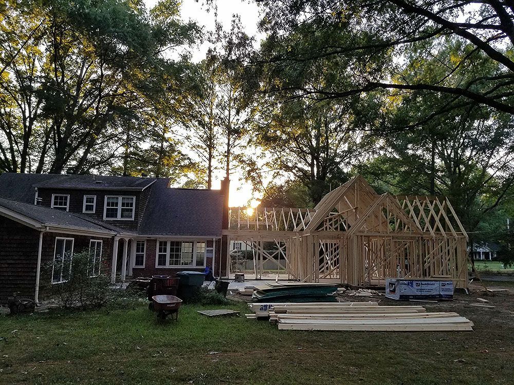 Exterior (In Progress) - House construction, new wooden frame addition. Sunlight through trees, yard with materials.