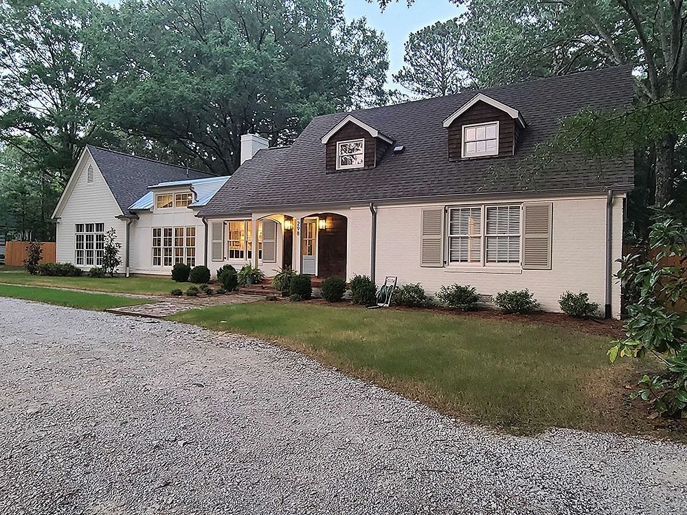 Exterior (After) - White house with dark roof and shutters, gravel driveway, and green lawn.