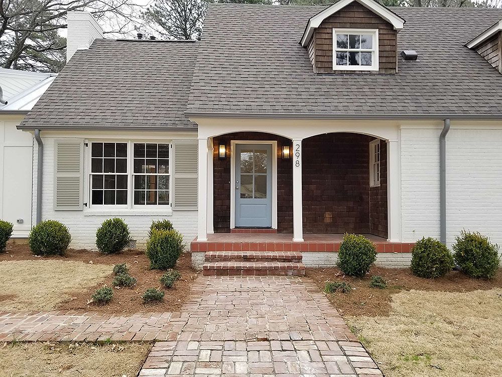 Front Door (After) - White house with brick walkway, blue front door, and small shrubbery in front.