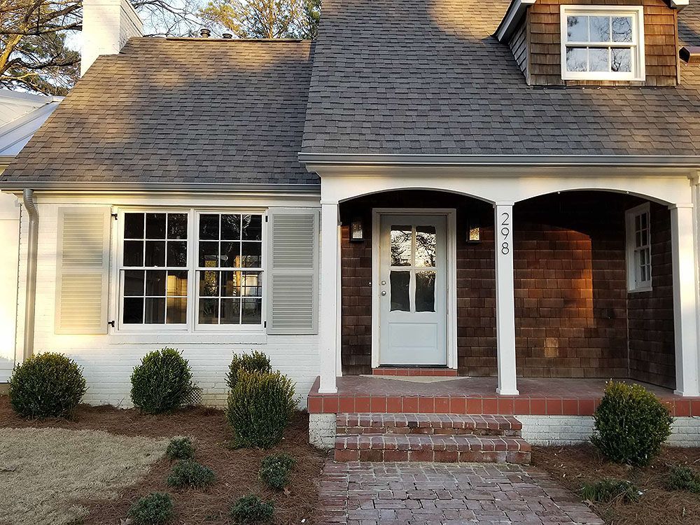 Front Door (After) - Cottage home with white trim, brown roof, and red brick porch; featuring a front door and windows.