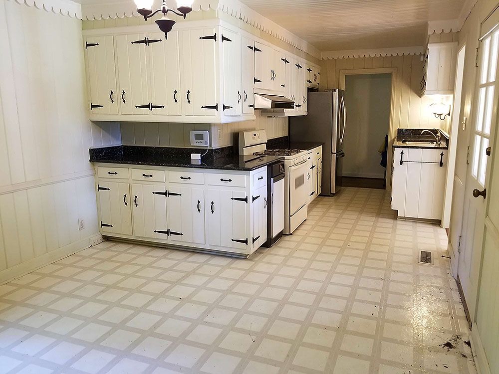 Kitchen (Before) - White kitchen with black accents. Cabinets, appliances, and tile floor.