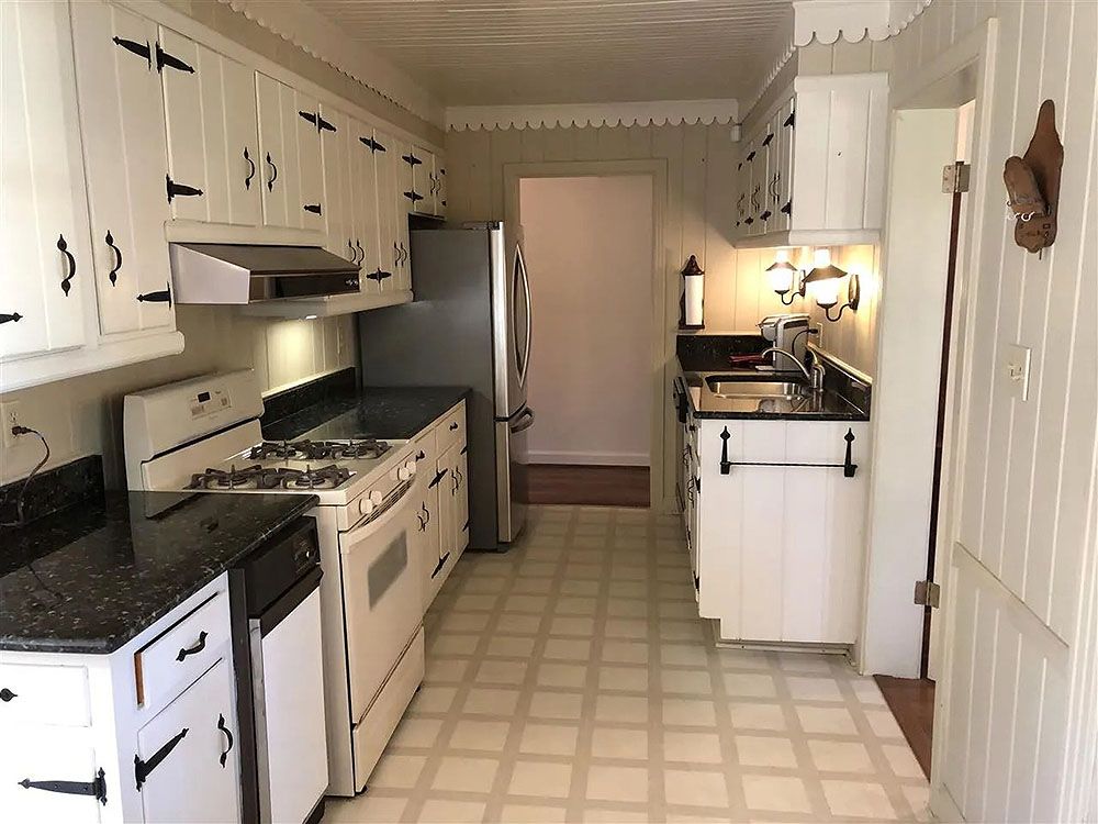 Kitchen (Before) - White kitchen with black countertops and appliances, including a stove and refrigerator.