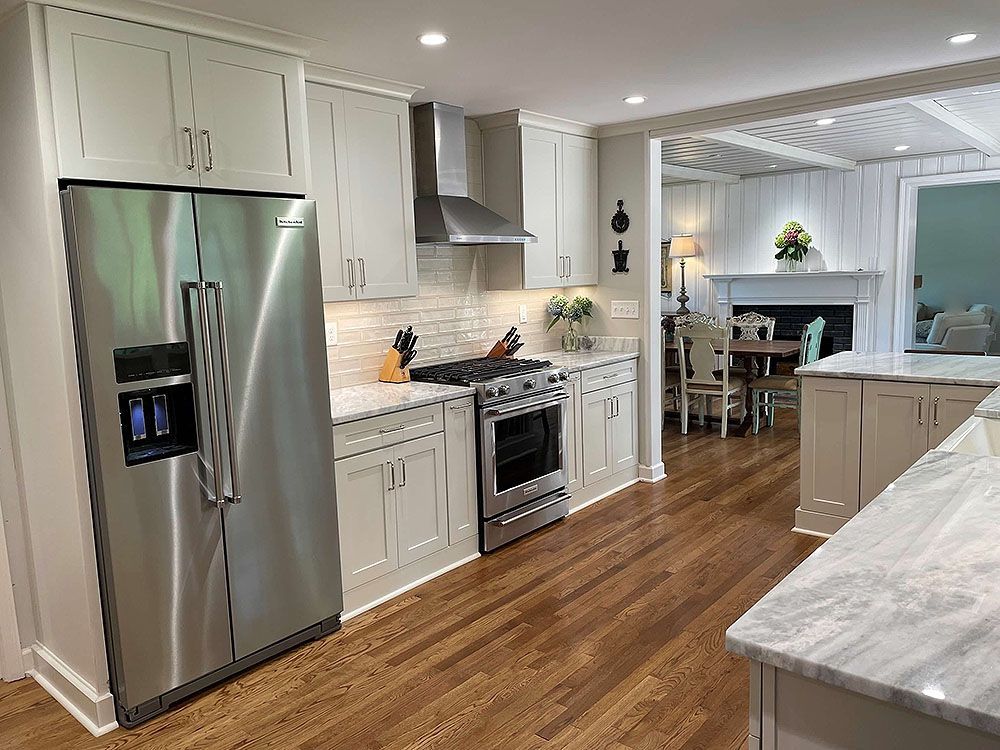 Kitchen (After) - A renovated kitchen with white cabinets, stainless steel appliances, and a view into a dining area.