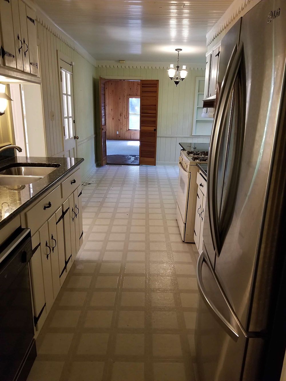 Kitchen (Before) - Kitchen with white cabinets, black countertops, stainless steel fridge, light green walls, and tile floor.