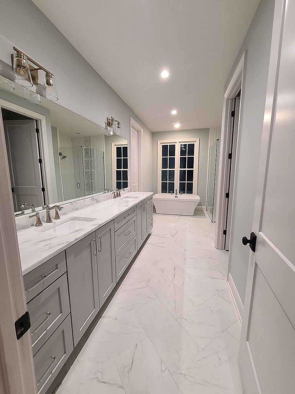 Master Bath 2 - Long, light blue and white bathroom with double sink vanity, bathtub, and windows.