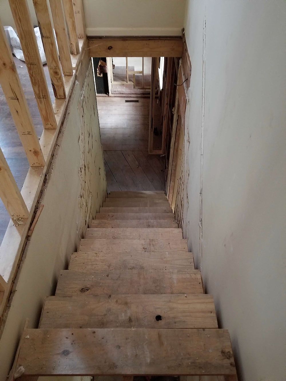 Stairs (In Progress) - Staircase under construction, leading down to a dark hallway, with exposed studs and unfinished walls.