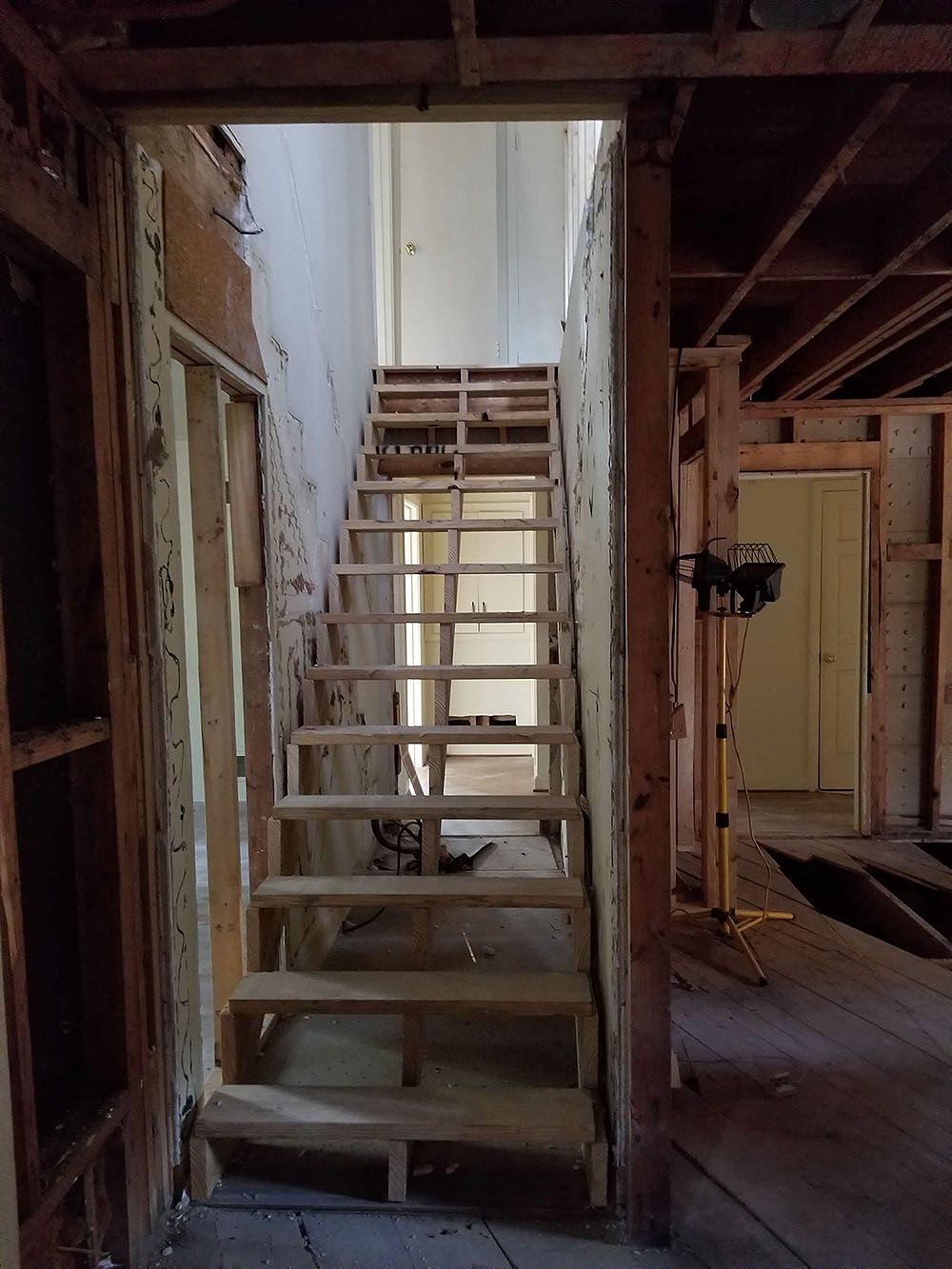 Stairs (In Progress) - Interior view of a partially constructed wooden staircase in a gutted house, leading to a hallway.
