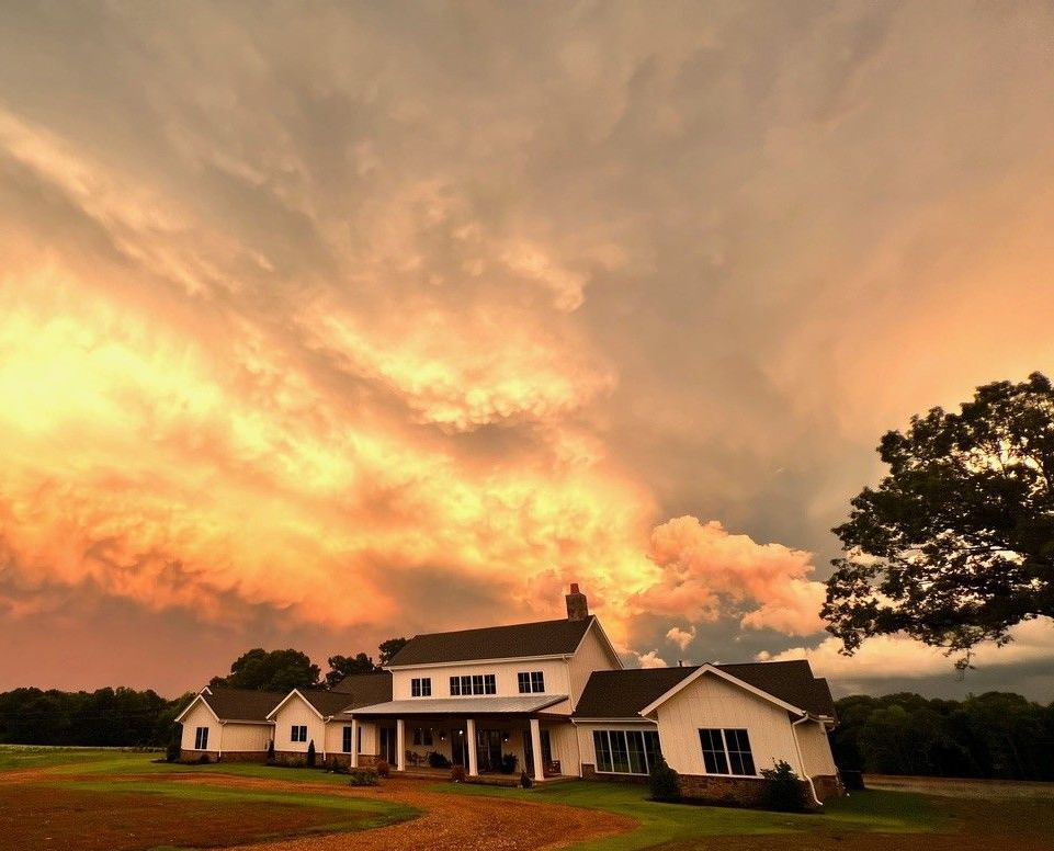 White farmhouse and outbuildings under a glowing orange sunset sky on a rural property