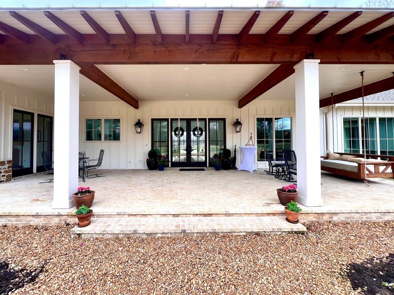 Covered front porch with white columns, glass doors, and potted plants on a gravel entryway.