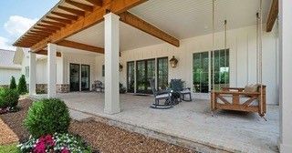 Covered patio with wooden pergola, white columns, glass doors, and outdoor seating beside a gravel garden