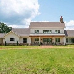 Large white farmhouse with a porch and chimney, set behind a wide green lawn under a blue sky