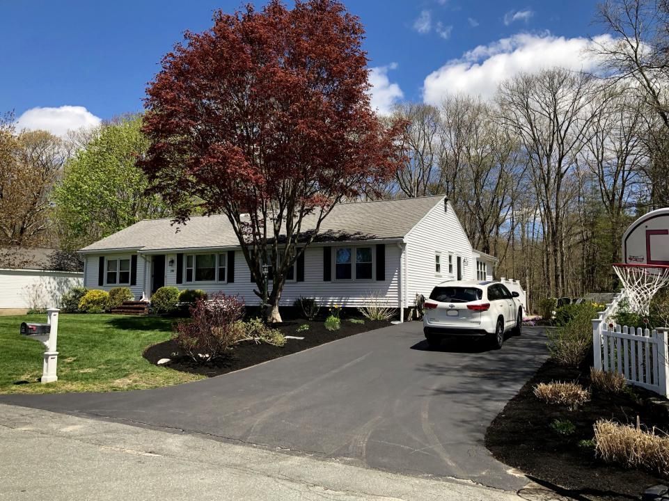 A white car is parked in front of a house with a basketball hoop in the driveway.