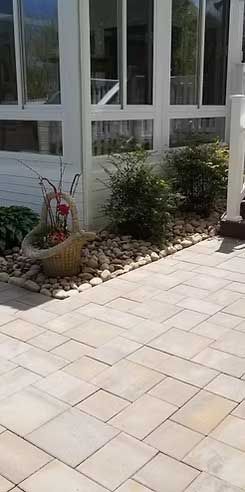 Exterior shot of a stone patio with decorative garden and glass windows in background.