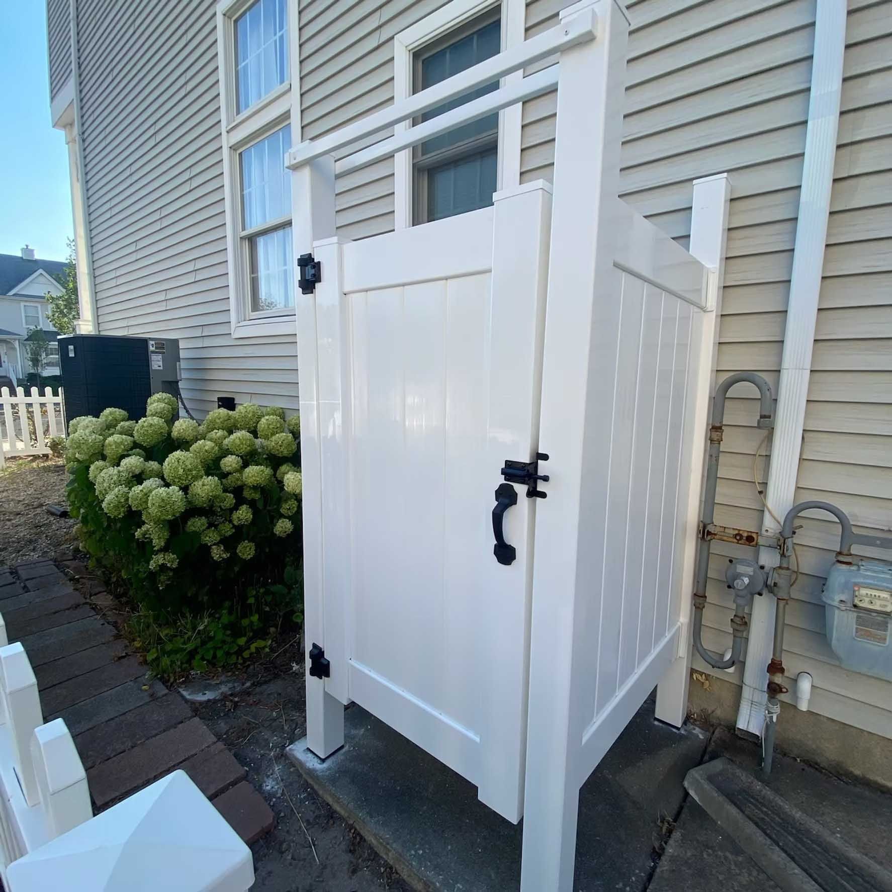 White outdoor shower against a light-colored house. It is next to a natural gas meter.