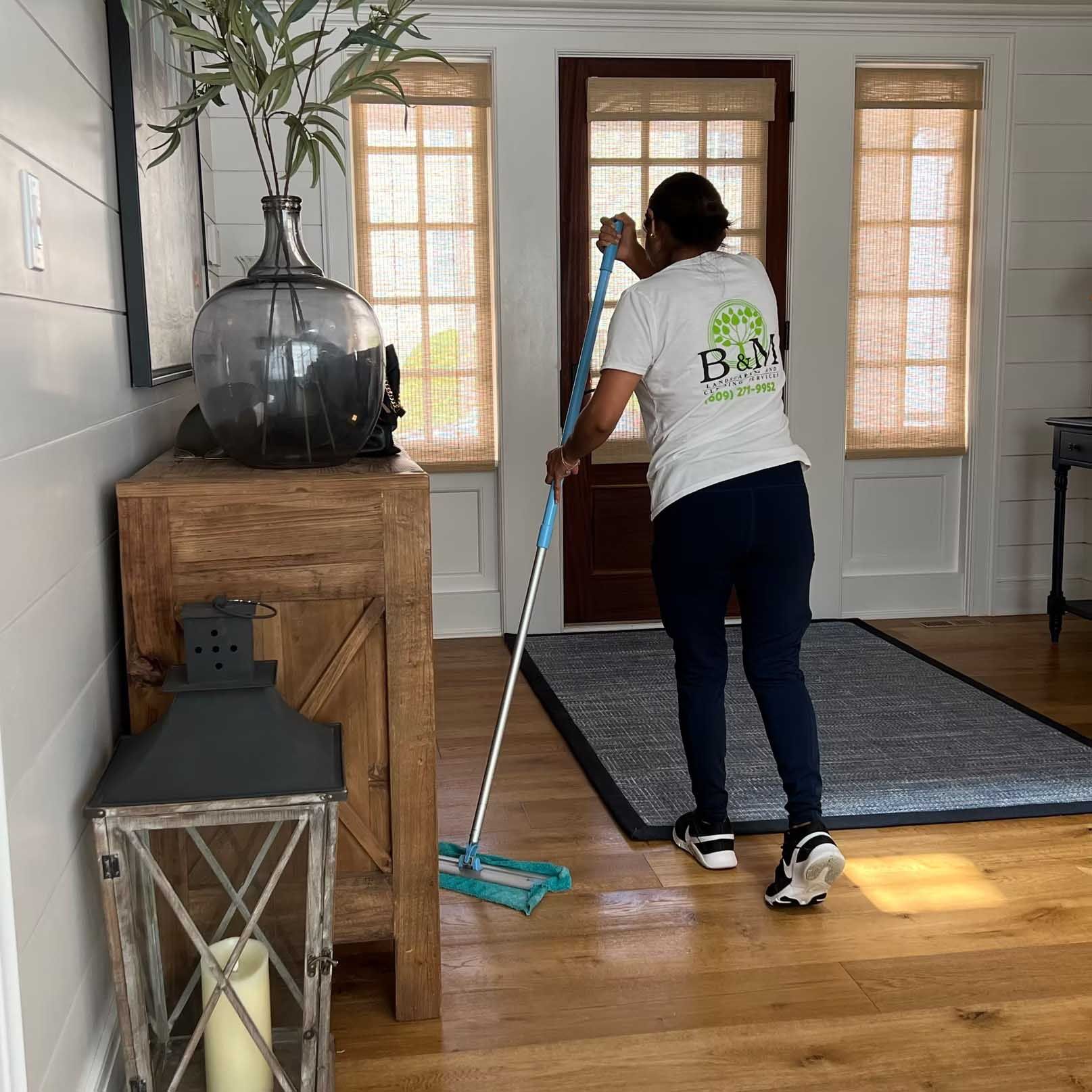 Person mopping hardwood floor in a well-lit hallway with a rug and wooden accents.