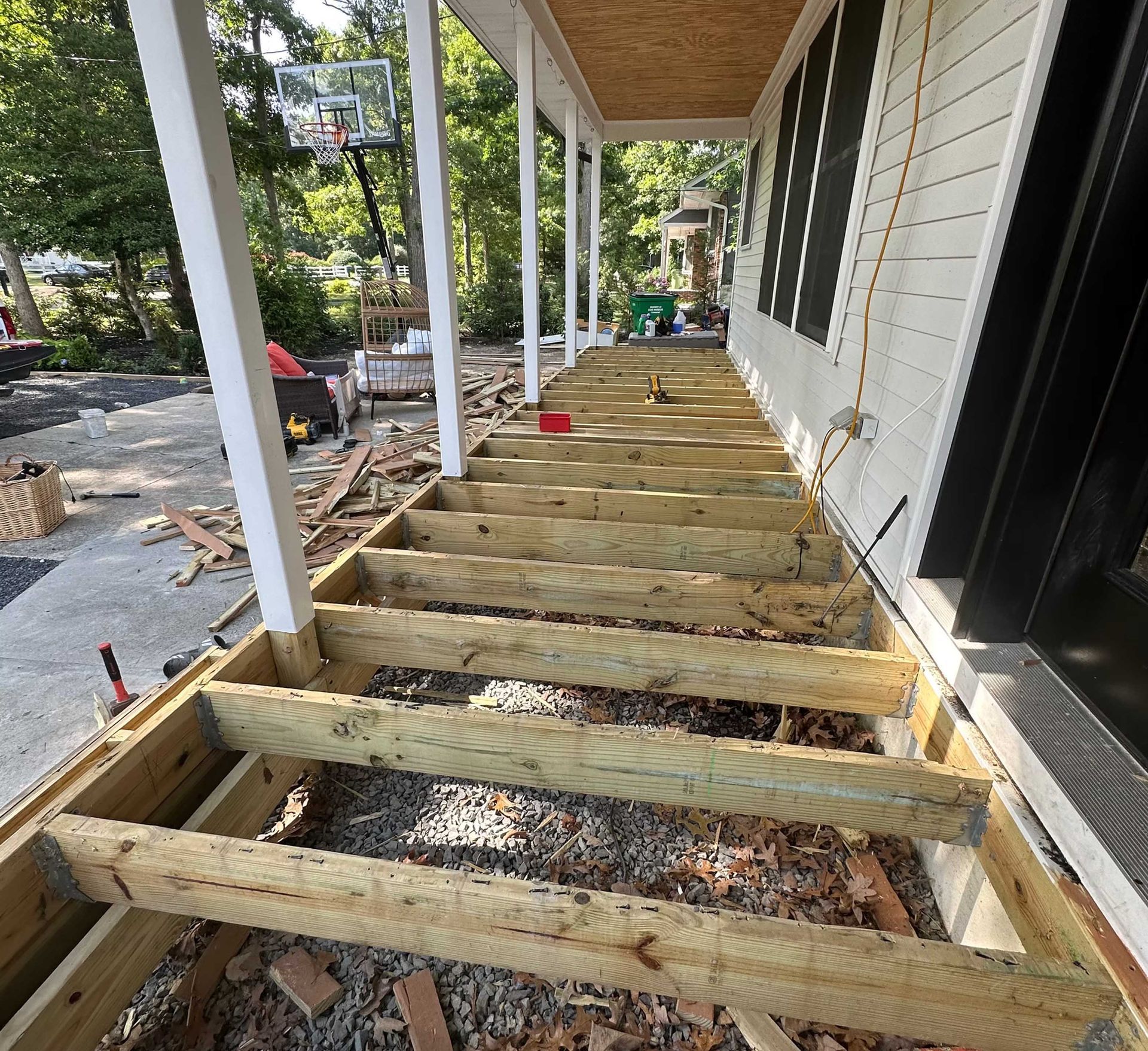 Porch under construction with exposed wooden frame. Gravel ground, white columns, and house siding.