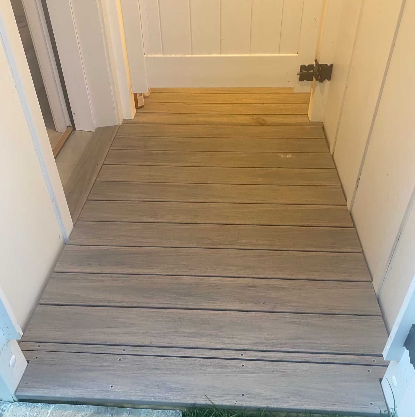 Wooden walkway between white walls, leading to a door; weathered gray planks.