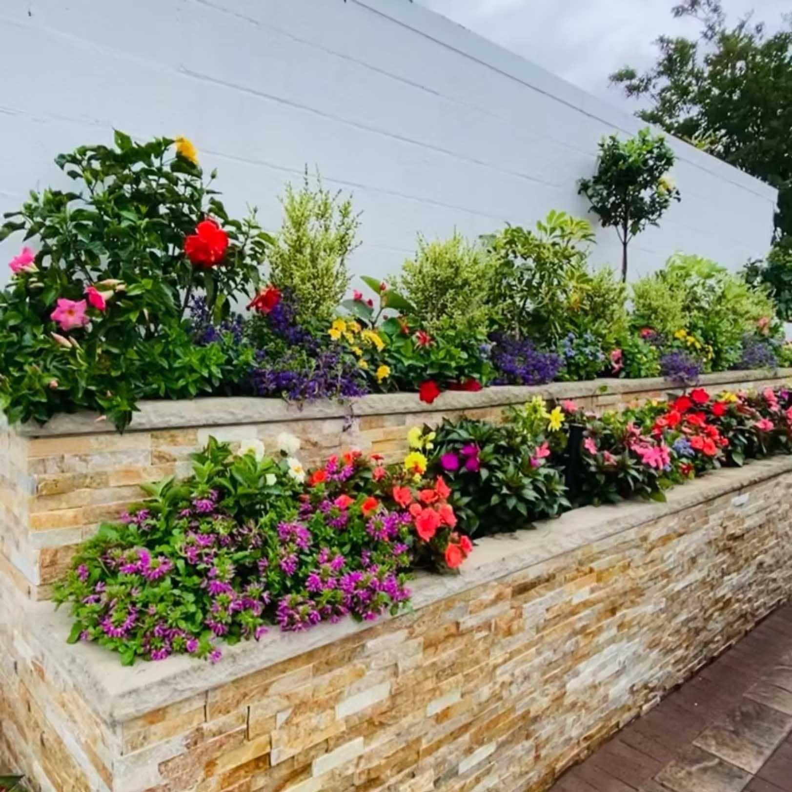 Stone tiered planter filled with colorful flowers against a white wall.