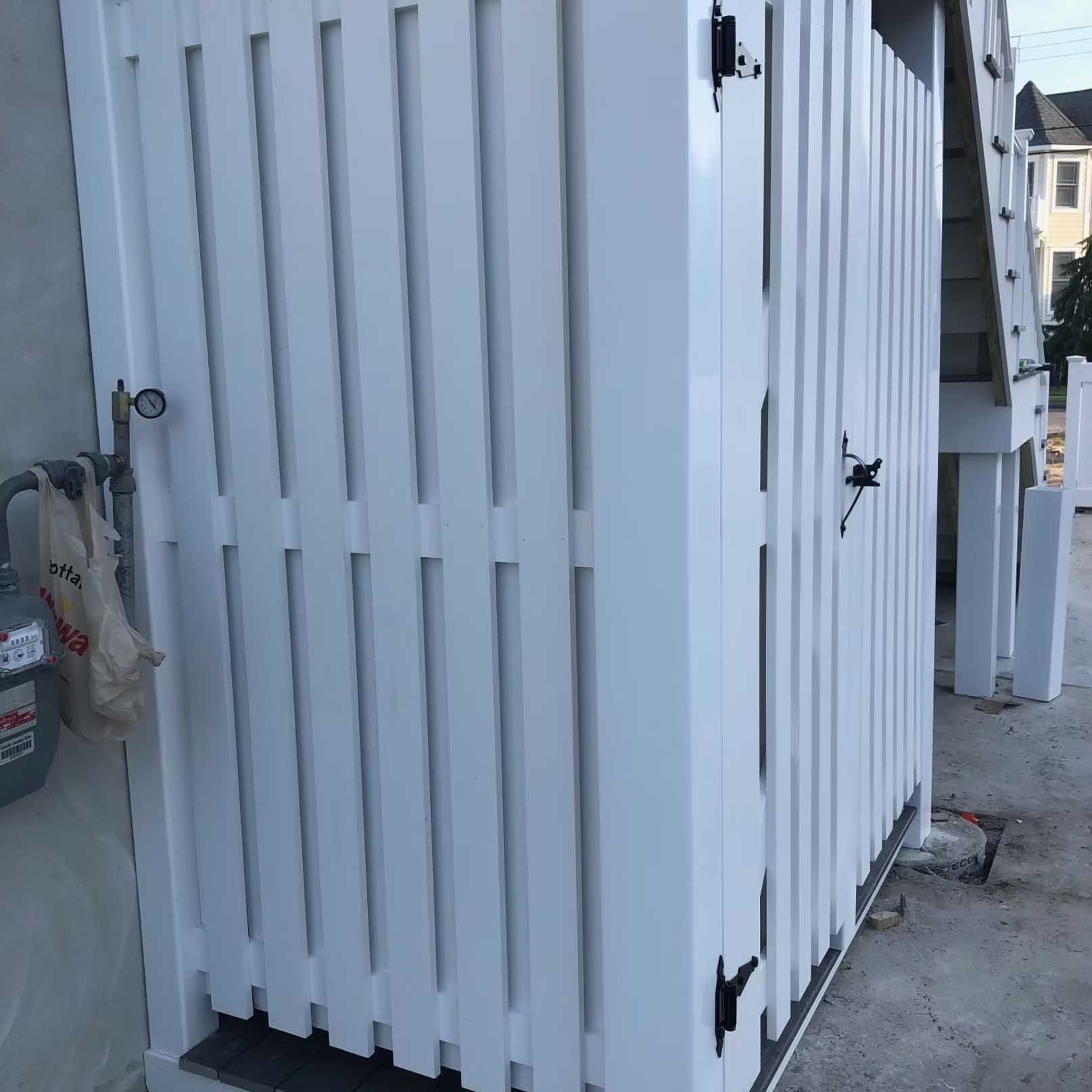 White outdoor shower enclosure with vertical slats, mounted next to a house wall.