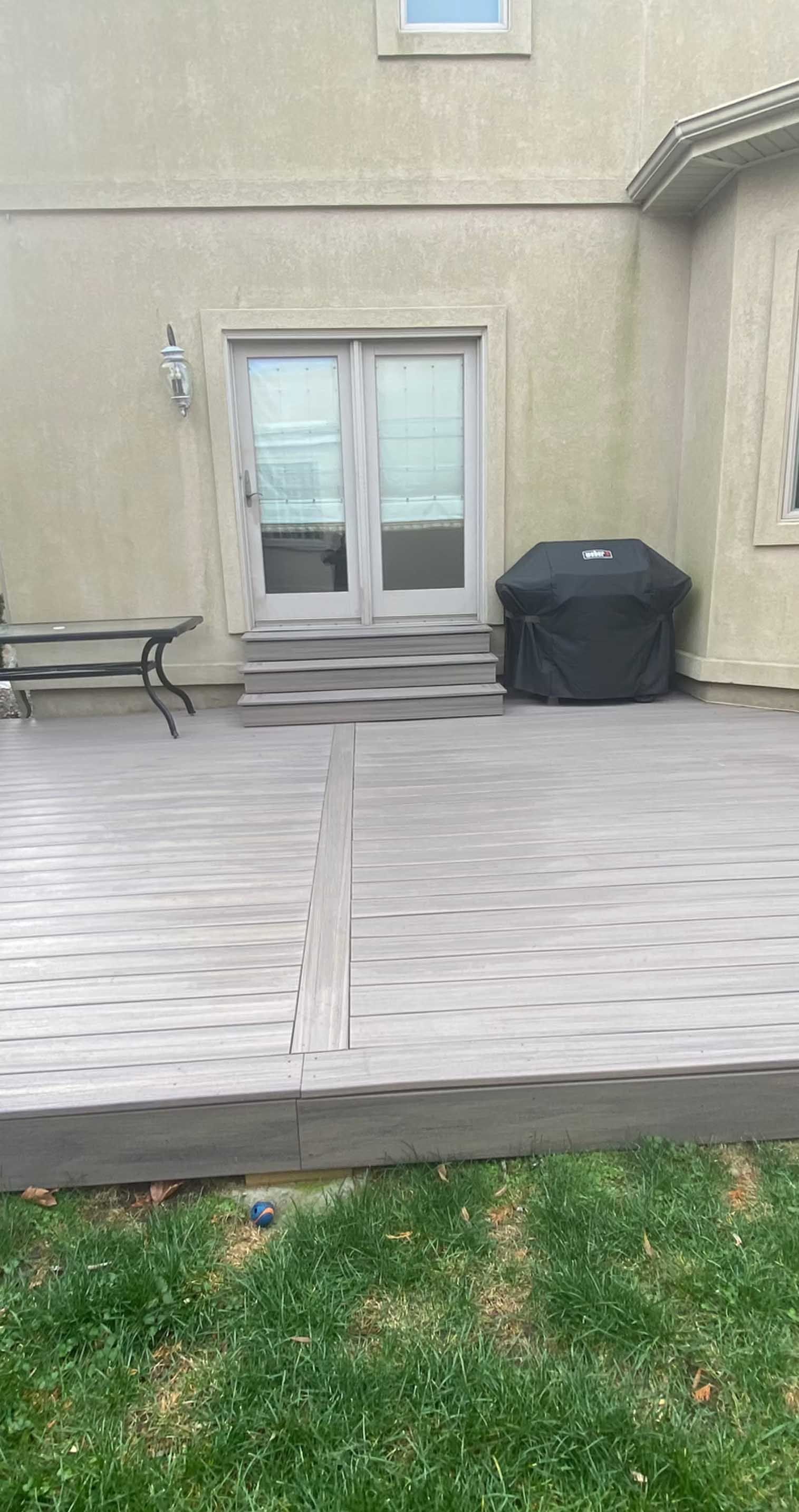 Backyard with a wooden deck, a covered grill, and double doors leading into a house.