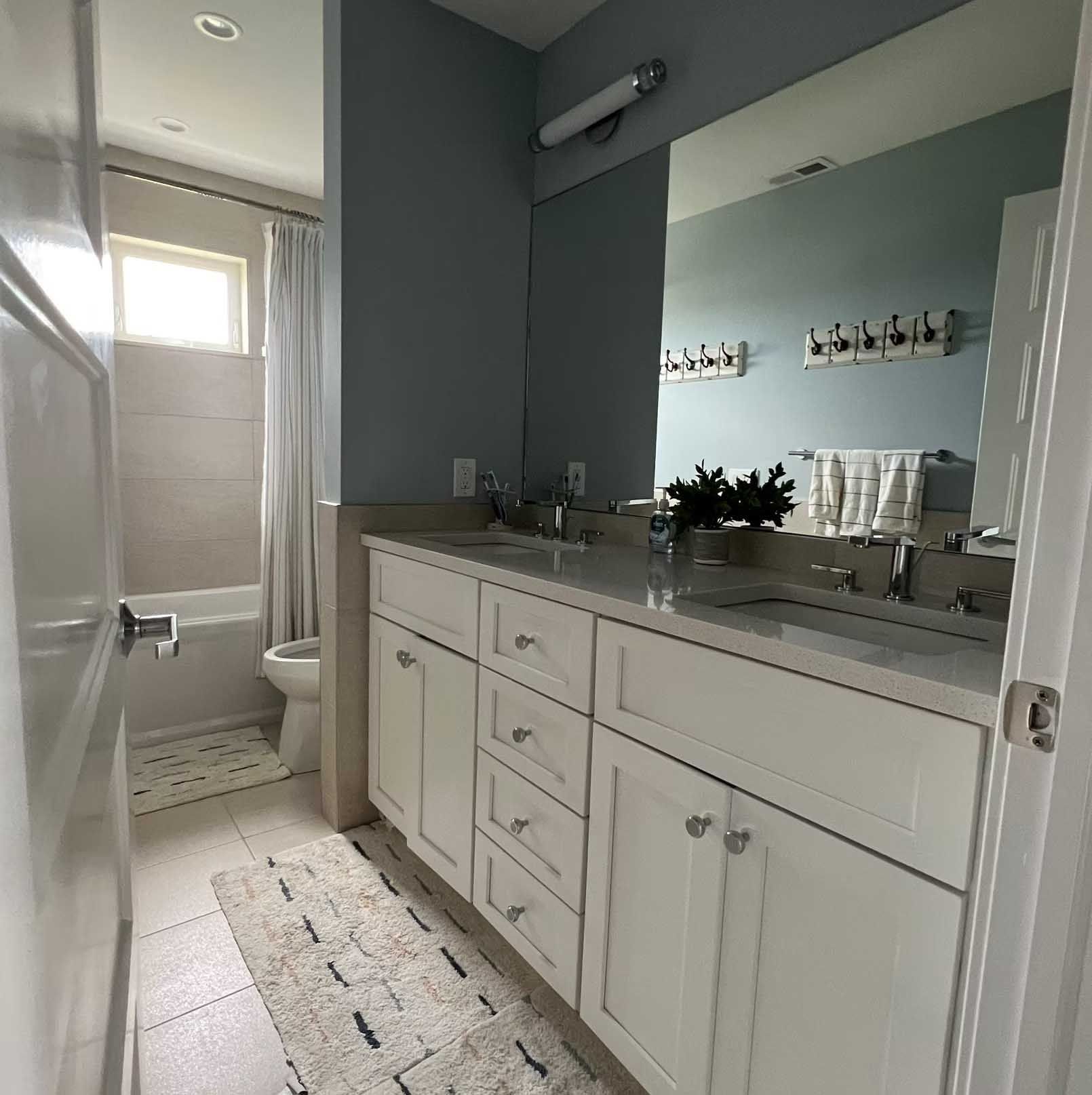 Bathroom with a white vanity, a large mirror, and a blue wall. A shower and toilet are visible.