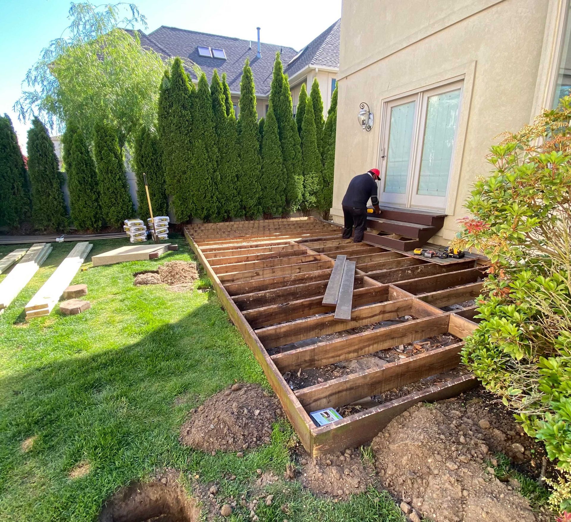 Deck construction in progress: Wooden frame, man working, attached to house, on green lawn.