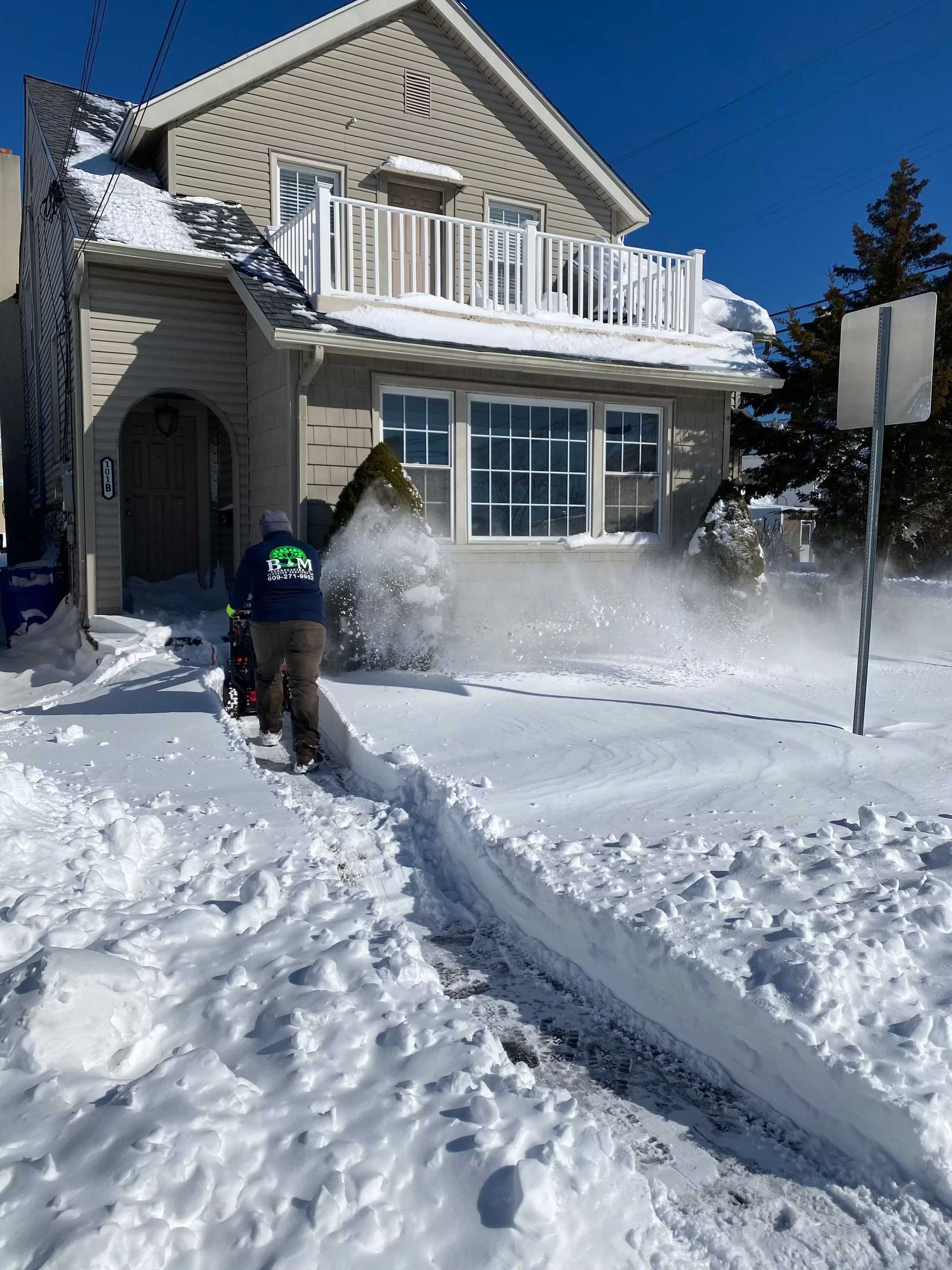 Person using snowblower to clear a snowy sidewalk in front of a house.