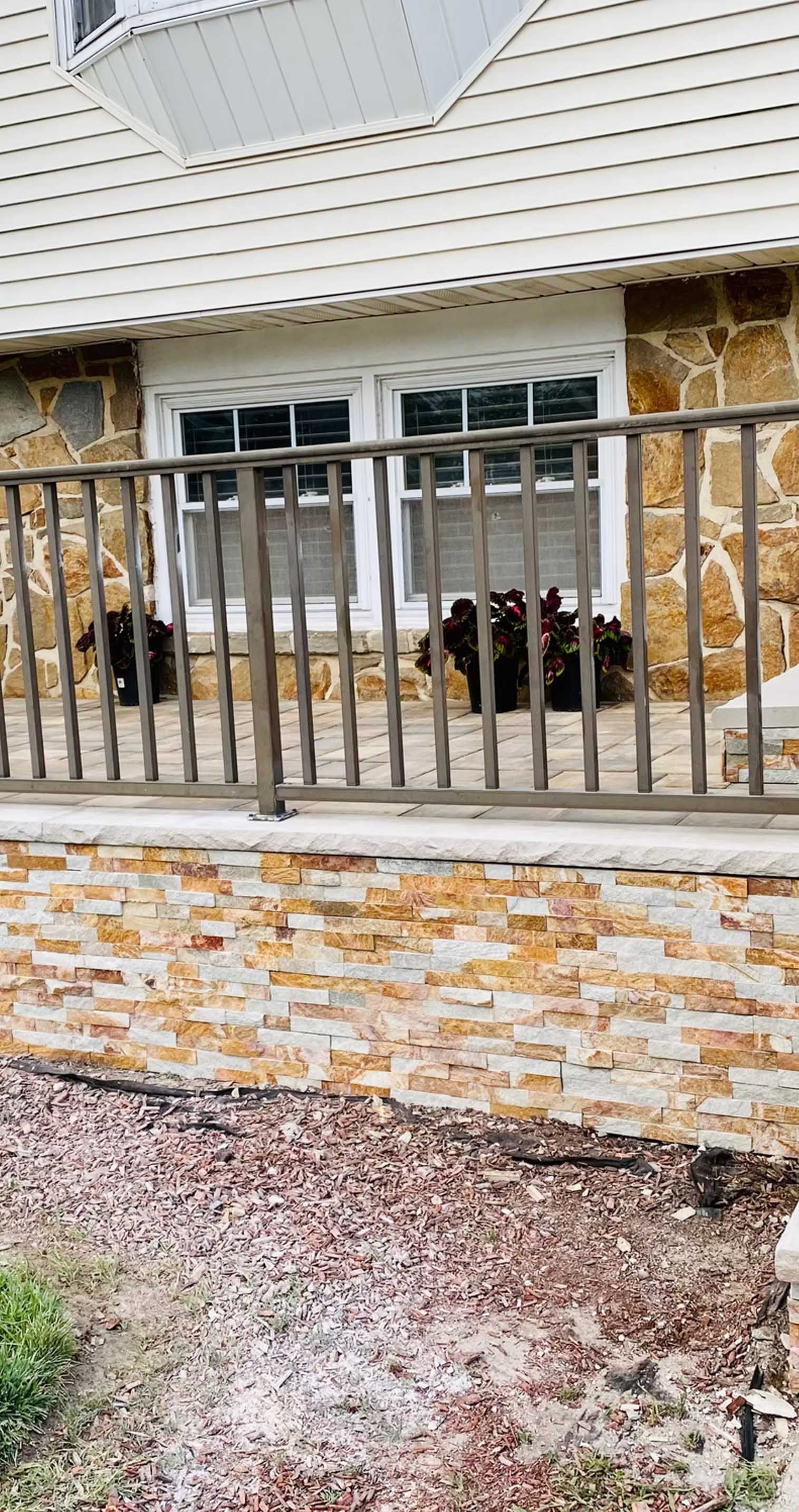 Exterior of a house with stone walls, white windows, and a wooden railing. Gravel and plants are in the foreground.