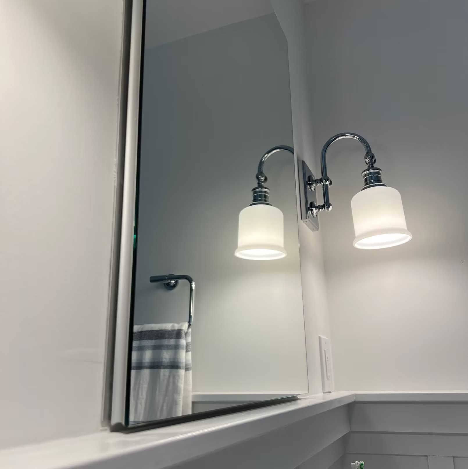 Bathroom mirror with wall-mounted lighting fixture. Towel rack and towel reflected in the mirror.
