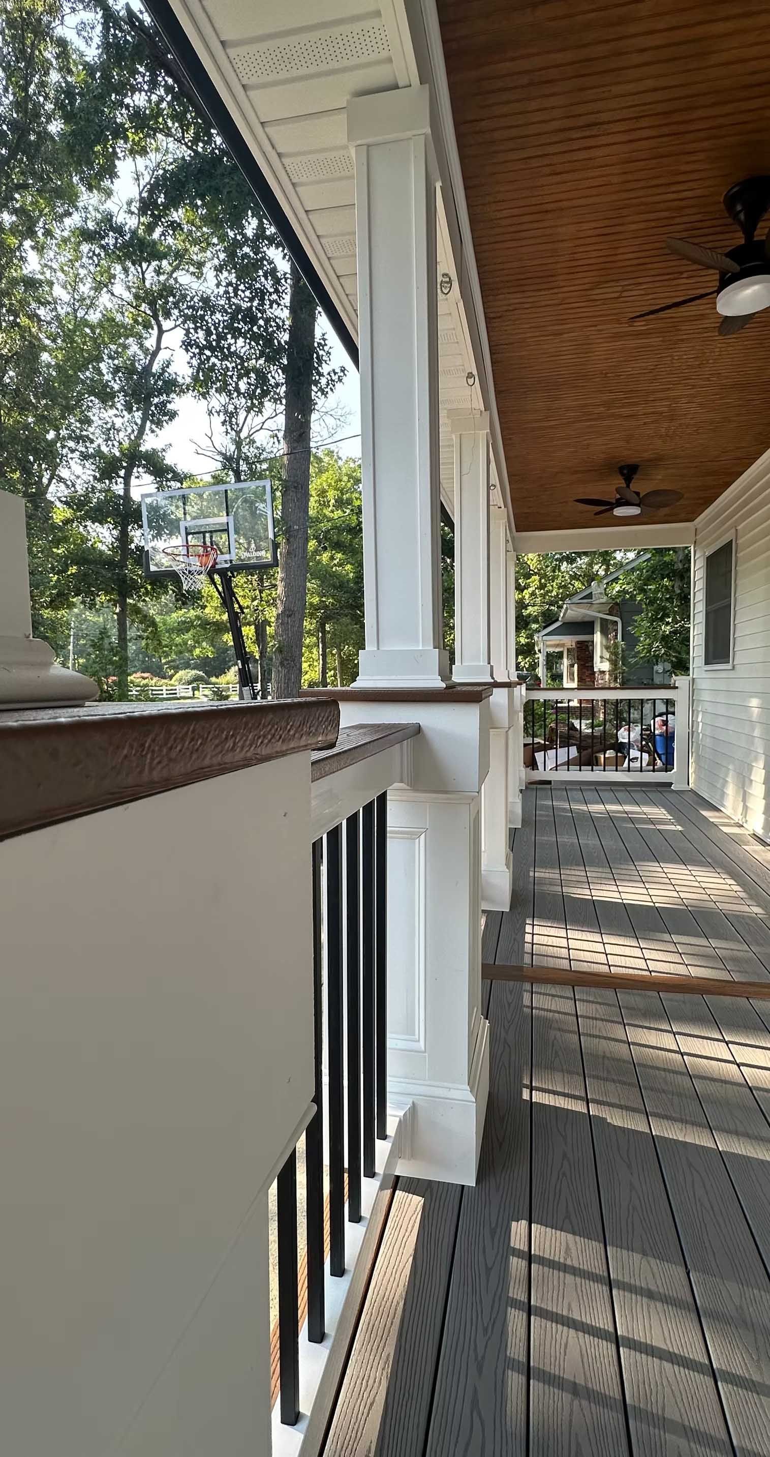 White porch with white columns, brown ceiling, black railing, and gray floorboards.