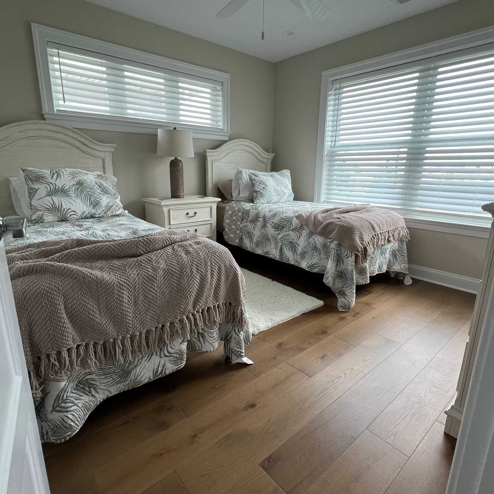Bedroom with two twin beds, wood floor, white furniture, beige walls, and window with blinds.