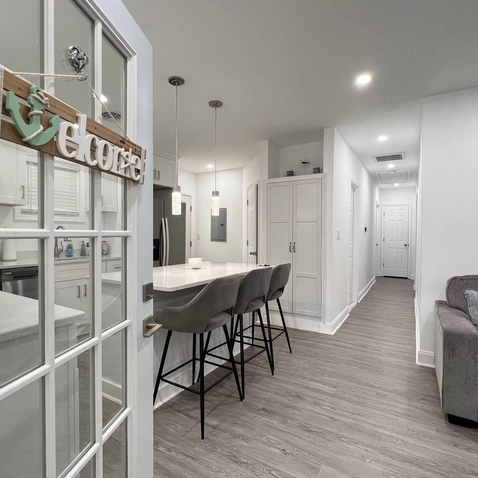 Open doorway to kitchen and hallway with a breakfast bar, gray flooring, and white walls.