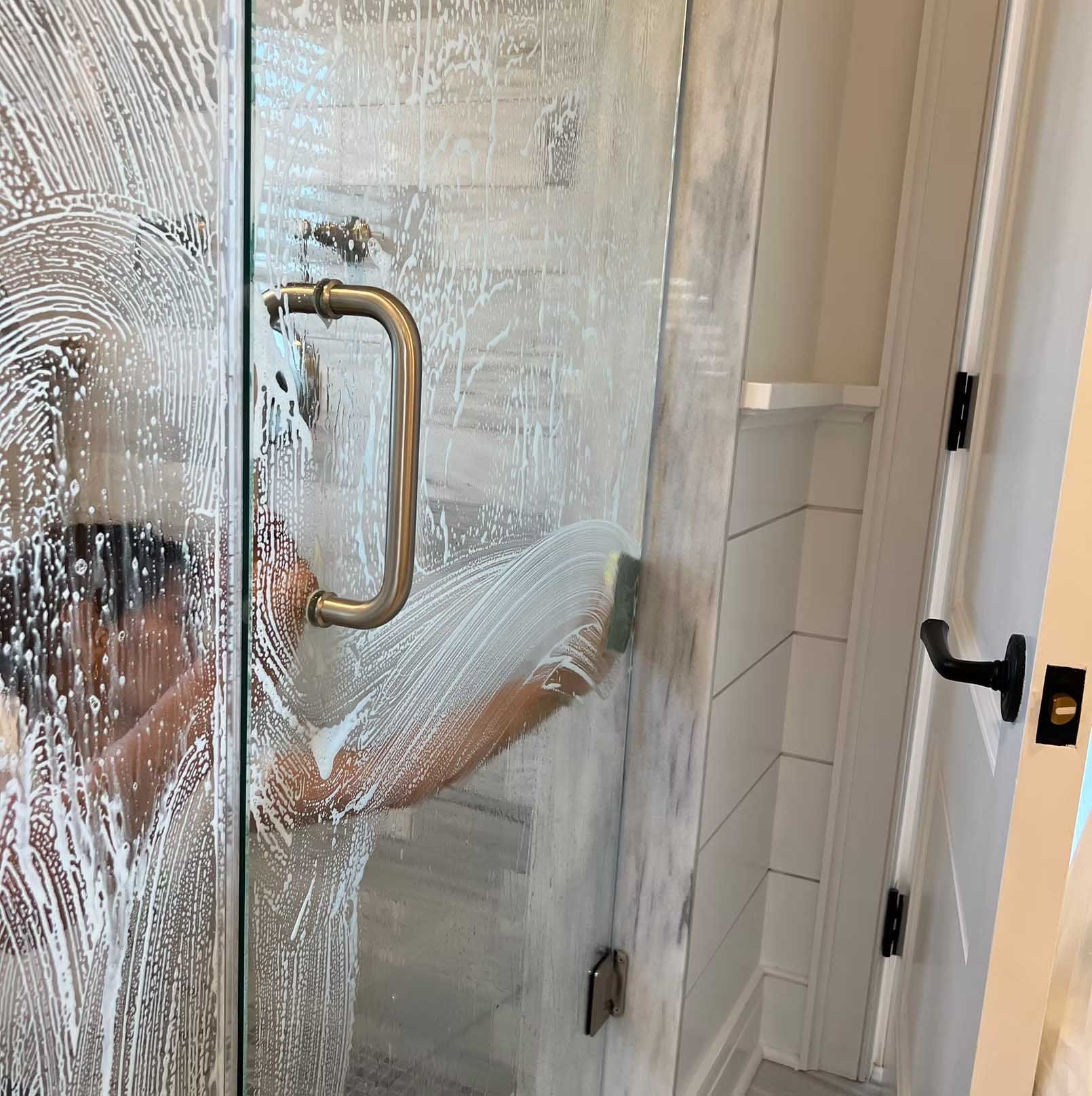 Person cleaning a glass shower door with soap and a sponge.