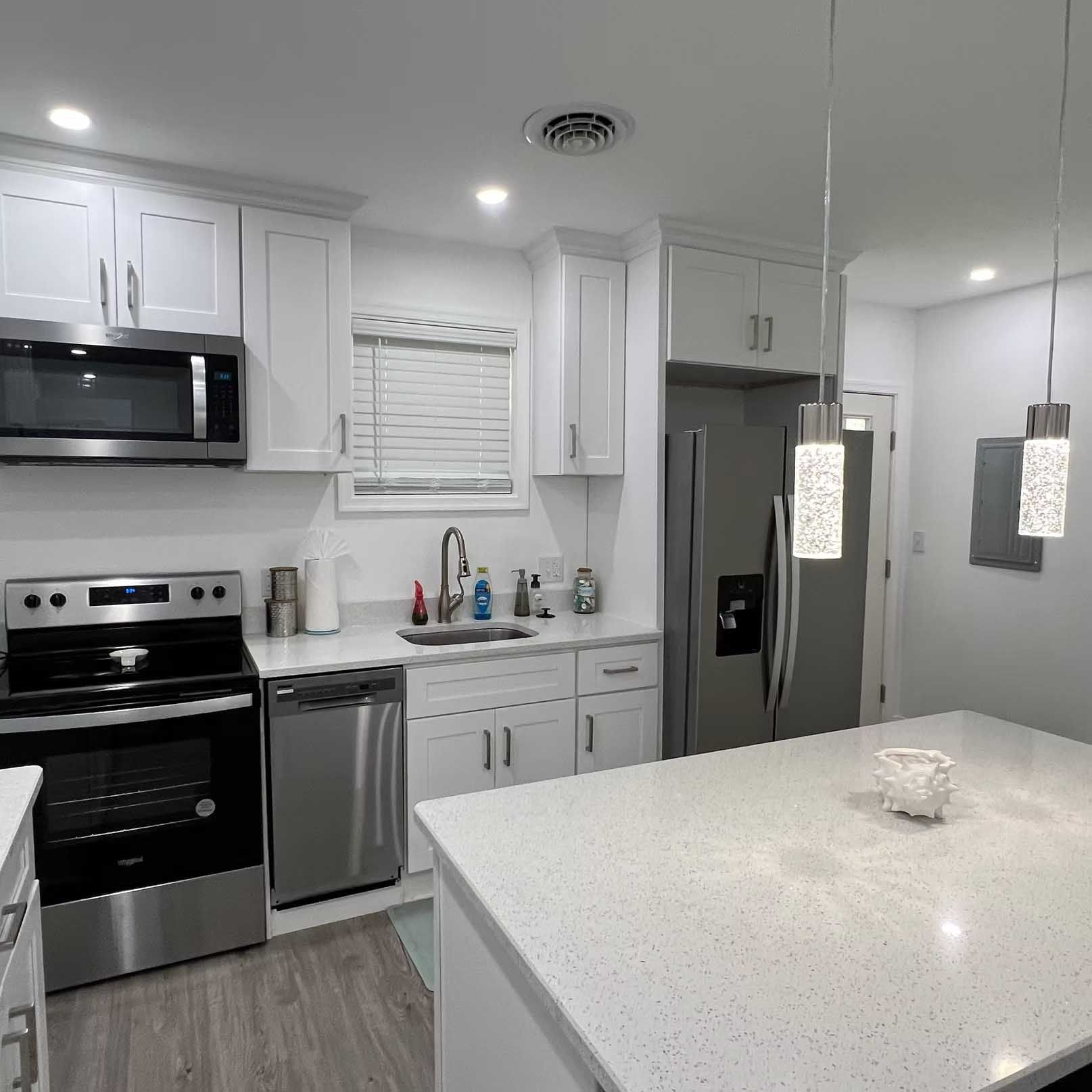 Modern white kitchen with stainless steel appliances, white countertop island, and pendant lights.