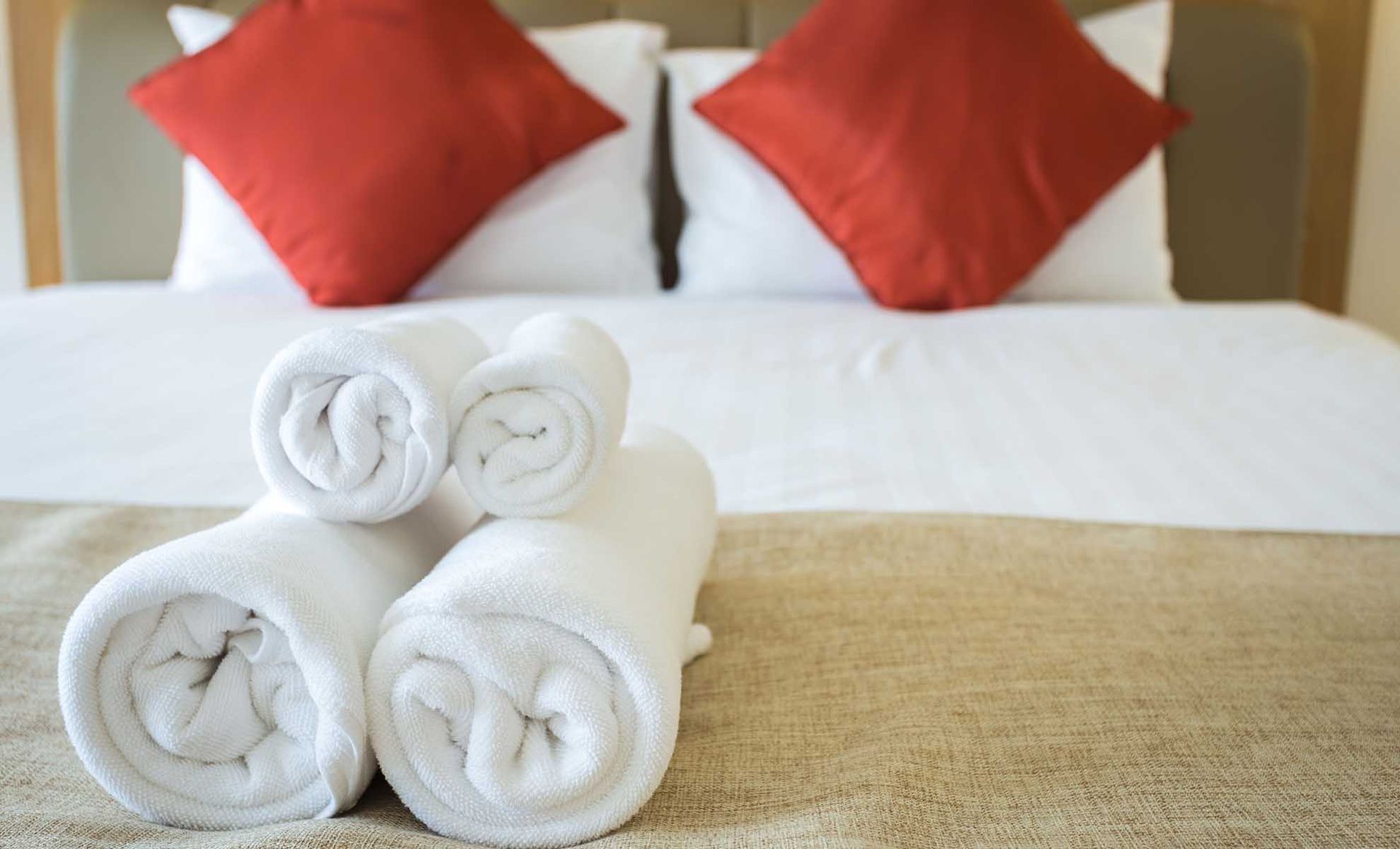 White rolled towels on a bed with red and white pillows.
