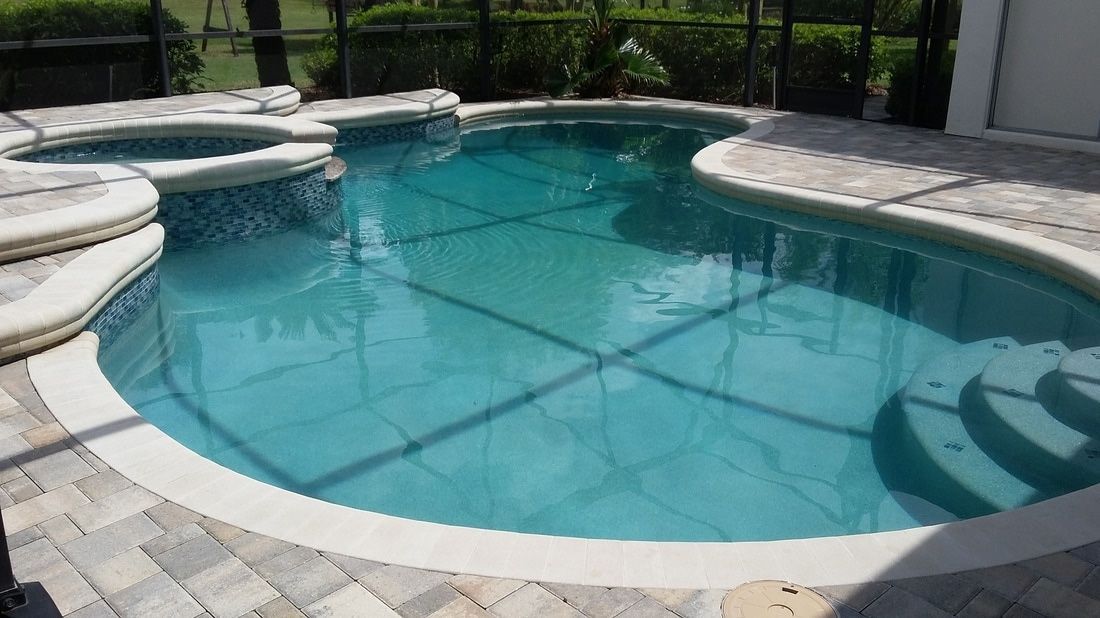 A turquoise swimming pool with a built-in spa and integrated steps, surrounded by light-colored stone pavers.