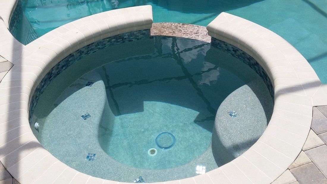 A round, light blue tiled hot tub set within a larger pool deck with light-colored coping.