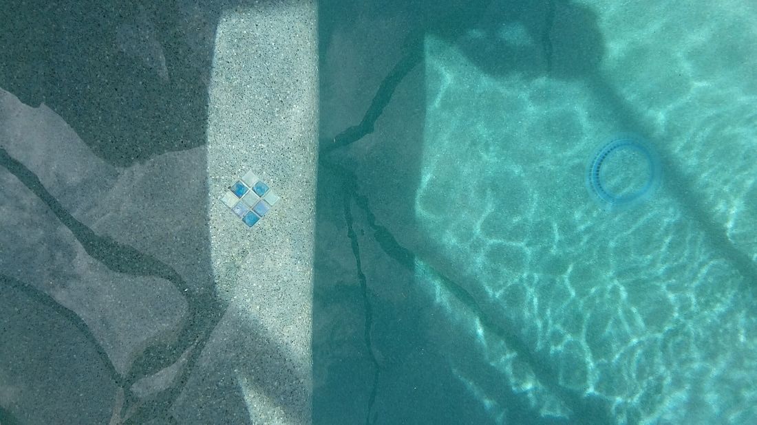 A split view of a pool, showing a dark, rough-textured edge next to clear, blue water with light ripples.