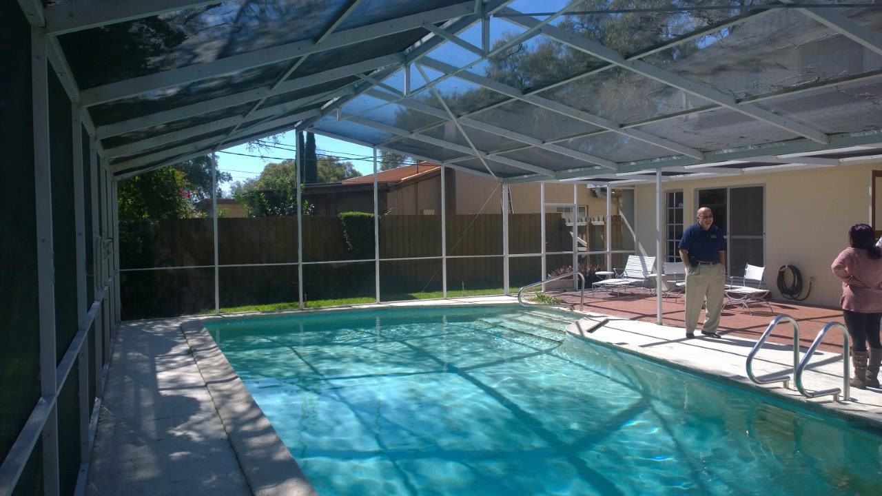 A screened-in swimming pool in a residential backyard with two people standing on the patio.