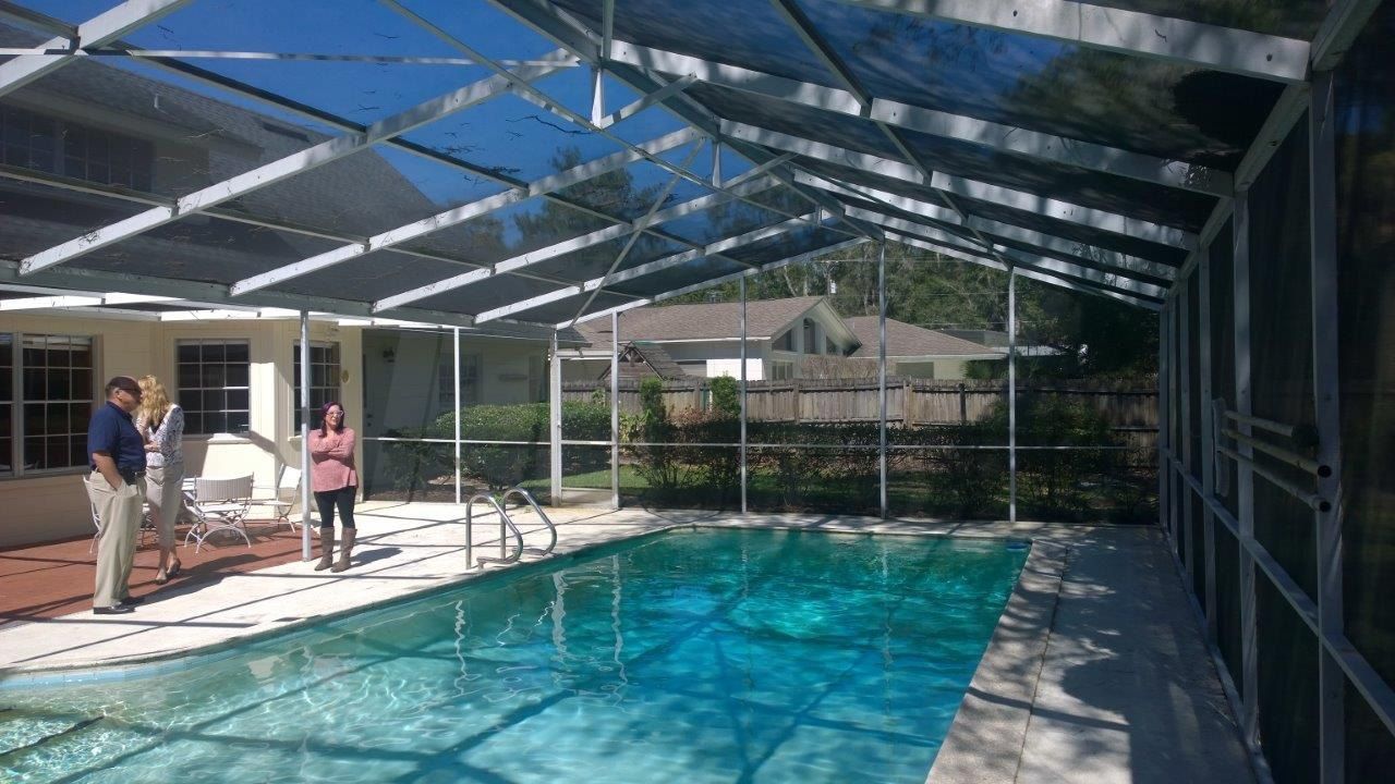 Three people stand on a pool deck enclosed by a metal-framed screen, with a swimming pool in the foreground.
